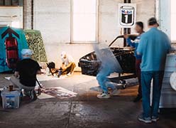 A group of artists in a warehouse painting the hoods of Porsche cars